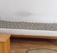 Ágy egy szobában fa mintázatú padlóval, mellette egy fa szekrény.