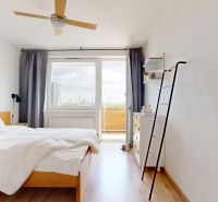Világos hálószoba ággyal, ventilátorral, fa mintázatú padlóval és erkéllyel a háromszobás lakásban.