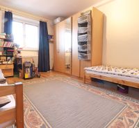Hálószoba nagy ággyal, szekrénnyel, szőnyeggel és fa dekoros padlóval egy kétszobás lakásban.