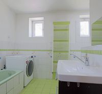 Családi ház fürdőszobája káddal, mosógéppel és mosdóval fehér-zöld árnyalatokban.