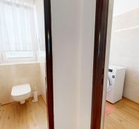 Fürdőszoba egy háromszobás lakásban WC-vel, mosógéppel és fa dekoros padlóval.