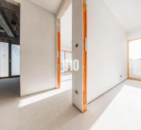 Tágas, befejezetlen 3 szobás lakás belső tere nagy ablakokkal és beton mennyezettel.