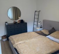 Hálószoba ággyal, komóddal és kerek tükörrel egy háromszobás lakásban.
