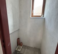 Kis szoba ablakkal egy családi házban, festetlen falak, csempe a padlón.
