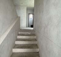 Betonlépcsők vezetnek az emeletre egy családi házban vakolt falakkal.