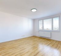 Tágas szoba nagy ablakokkal és fa dekorációjú padlóval egy háromszobás lakásban.