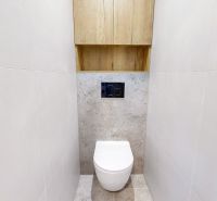 Fehér csempés falú WC egy háromszobás lakásban, WC fölötti szekrénnyel.