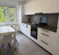 Konyha kétszobás lakásban szürke padlóval és fehér szekrényekkel.