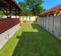 A családi ház kertje Darnózseliben gyepes, pergolával és fákkal körülvéve.