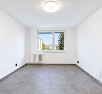 Tágas szoba ablakkal, radiátorral és fa dekorációjú padlóval egy kétszobás lakásban.