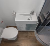 A fürdőszoba zuhanyzót, mosdót és WC-t tartalmaz, padlója fa dekorációval van ellátva.