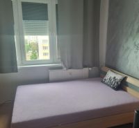 Hálószoba egy háromszobás lakásban ággyal és szürke dekoratív párnával.