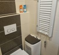 Fürdőszoba WC-vel egy háromszobás lakásban, krém-barna csempe és tárolóhely.