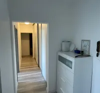 Folyosó egy kétszobás lakásban fehér komóddal és fa mintázatú padlóval.