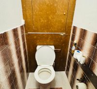 Háromszobás lakás WC-je barna csempékkel és lábtörlővel.