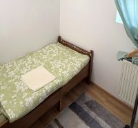 Egyszemélyes ágy, ruhatartó állvány, zöld függönyök, fa mintázatú padló.