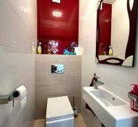Fürdőszoba egy háromszobás lakásban függesztett WC-vel, mosdóval és piros csempékkel.