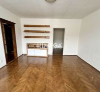 Szoba egy háromszobás lakásban, fa mintázatú padlóval és polcokkal a falon.