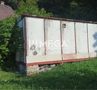 Egy régi raktár az utcai kertben Humennóban, zöldnövényzettel és növekvő fűvel körülvéve.
