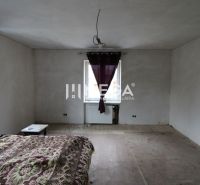Hálószoba egy családi házban, hámló padlóval és lila függönyökkel.