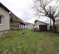 Családi ház kertje a Pakostov utcában, egy régebbi fa fészerrel és gyepfelülettel.