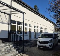 Épület üzlethelyiségekkel a humennéi Tyršova utcán, parkoló autók, fa.