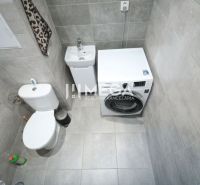 Fürdőszoba egy háromszobás lakásban mosógéppel és WC-vel, szürke árnyalatokban.