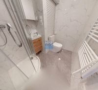 Fürdőszoba garzonlakásban káddal, mosdóval, WC-vel és márvány dekoros falakkal.