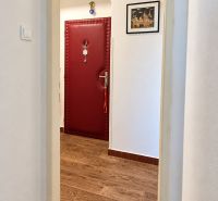 Folyosó piros ajtókkal és fa mintázatú padlóval egy háromszobás lakásban.