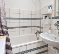 Fürdőszoba káddal, mosdóval, fehér csempével és mintás részletekkel egy háromszobás lakásban.
