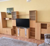 Nappali egy háromszobás lakásban, fa hatású padlóval, világos bútorokkal, televízióval.