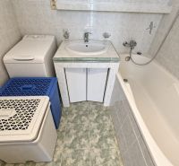Fürdőszoba mosdókagylóval, káddal és mosógéppel egy háromszobás lakásban, világos árnyalatú csempékkel.