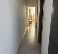 Keskeny folyosó csempézett padlóval vezet egy világos szobába egy kétszobás lakásban.