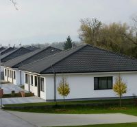 Sötét tetős családi házak Hôrka nad Váhom településen, zöldövezettel és úttal körülvéve.