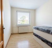 Világos szoba egy háromszobás lakásban, fa dekorációs padlóval és ággyal.