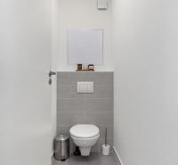 Keskeny WC fehér falakkal és szürke csempékkel egy kétszobás lakásban.
