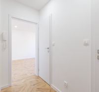 Folyosó egy kétszobás lakásban, fa mintázatú padlóval és fehér falakkal.