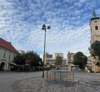 Üzlethelyiségek Topoľčanyban, kövezett térrel és háttérben egy templommal.