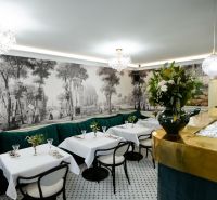 Kereskedelmi helyiségek belső tere fehér asztalokkal, zöld kanapékkal és falfestményekkel.
