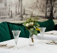 Elegánsan megterített asztal fehér terítővel, virágokkal teli vázával és kristálypoharakkal.