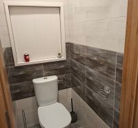 Fürdőszoba egy egyszobás lakásban WC-vel, sötétebb tónusú csempékkel burkolva.