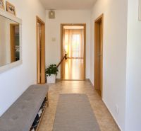 Folyosó egy családi házban csempével, cipőspaddal és tükörrel.