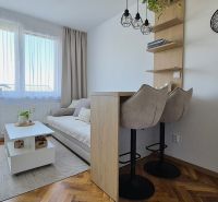 Garzonlakás kanapéval, asztallal, bárszékekkel és fa dekorációjú padlóval.