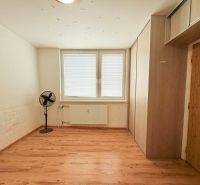 Szoba fa dekorációs padlóval, ventilátorral és tárolóhellyel egy háromszobás lakásban.