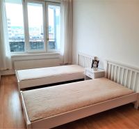 Hálószoba két ággyal, éjjeliszekrénnyel és fa dekoros padlóval egy kétszobás lakásban.