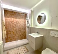 Fürdőszoba walk-in zuhanyzóval, fali WC-vel és megvilágított tükörrel egy garzonlakásban.