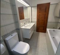 Fürdőszoba káddal és WC-vel egy családi házban, fehér csempékkel és faajtókkal.