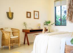 Világos hálószoba családi házban, rattan székkel és fa asztallal.