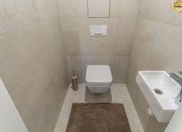 Függesztett WC-vel, kis mosdóval és bézs csempével ellátott WC, Lakásépítés.