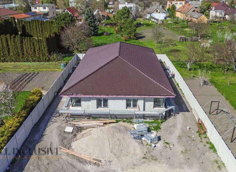 Rodinný dom s hnedou strechou, záhrady a stavebné materiály na dvore.